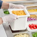 A person in gloves holding a Carlisle Coldmaster food pan full of cherry tomatoes.