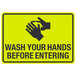 A yellow sign with black text and hands washing that says "Wash Your Hands Before Entering"