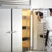 A man in a chef uniform opening a Traulsen G Series reach-in refrigerator with right hinged doors.