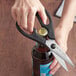 A hand using Mercer Culinary multi-purpose shears to open a bottle of beer.