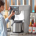 A woman using an Estella Caffe airpot coffee maker on a counter.