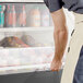 A man in an apron opening the door of a black Avantco air curtain merchandiser.