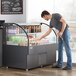 An Avantco black horizontal air curtain merchandiser on a counter with a man standing nearby.