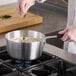 A hand stirring food in a Choice aluminum sauce pan on a stove.