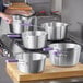 A person holding a Choice Tapered Aluminum Sauce Pan with a purple silicone handle.