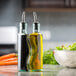 A Tablecraft clear glass oil and vinegar cruet set on a counter with a bowl of salad.