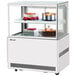 A Turbo Air white refrigerated bakery display case with cakes and desserts on two tiers.