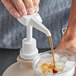 A hand using a Mountain Cider Company syrup pump to pour brown liquid into a cup.