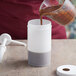 A person pouring brown liquid from a measuring cup into a white Tablecraft PourMaster container.