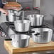 A person using a Choice aluminum sauce pan with a black handle to cook in a kitchen.