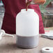 A person pouring brown liquid into a white Tablecraft plastic container.