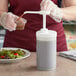 A person using a Tablecraft condiment pump to pour brown liquid into a white container.