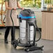 A woman in an apron using a Lavex stainless steel wet/dry vacuum in a professional kitchen.