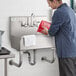 A man washing his hands in a Regency stainless steel utility sink.