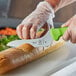 A person using a Mercer Culinary Ultimate White bread knife to cut a loaf of bread.