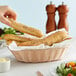 A person holding a Tablecraft oval natural-colored bread basket filled with bread.