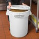 A woman holding a large white Baker's Mark ingredient storage bin with a lid full of food.