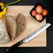 A Shun Classic bread knife slicing a piece of bread on a cutting board.