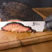 A hand holding a Shun Classic brisket knife over a piece of meat on a cutting board.