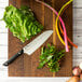 A Kai PRO Santoku knife next to leafy and root vegetables on a cutting board.