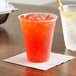 A plastic cup of orange liquid with ice on a table.