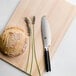 A Shun Classic forged utility knife cutting bread on a cutting board.