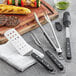 Wusthof barbecue tongs with black and white handles next to a fork and a knife.