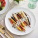 A white Acopa Condesa porcelain plate with a meal of carrots and salad on it.