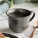 An Acopa Armor Gray porcelain cup of coffee with a spoon on a table.
