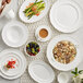 A white Acopa porcelain mug on a table with white plates and bowls.