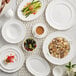 A table set with Acopa Condesa pearl white saucers and bowls with coffee and food.