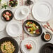 A table with Acopa Condesa white porcelain plates, bowls, and cups on it.