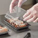 A person in gloves putting food into a Choice medium rectangular food container.