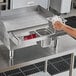 A man holding a Universal 24" Griddle Condiment Rail on a stainless steel counter.