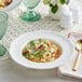 A bowl of tortellini soup with cheese in a white Acopa porcelain bowl.