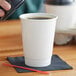 A hand holding a white lid over a white Choice paper hot cup of coffee.