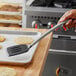 A hand using a Tablecraft black slotted spatula to lift food from a pan.