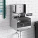 A Regency wall mounted hand sink with side splashes, paper towel, and soap dispenser above it.