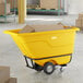 A yellow heavy-duty tilt truck or trash cart with a 0.5 cubic yard capacity, loaded with cardboard boxes.
