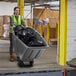 A woman in a green vest pushing a Lavex grey wheelbarrow full of garbage.