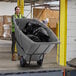 A woman in a safety vest pushing a Lavex grey trash cart full of garbage.