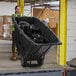 A woman in a yellow vest pushing a black Lavex heavy-duty tilt truck full of garbage.