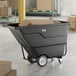 A black heavy-duty tilt truck or trash cart with a 1 cubic yard capacity, loaded with cardboard boxes.