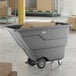 A gray Lavex 1 cubic yard light-duty tilt truck or trash cart with an 850 lb. capacity, shown holding cardboard boxes in a warehouse setting.