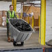 A woman in a safety vest pushing a grey Lavex tilt truck full of black garbage bags.