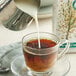 A glass cup of coffee with Elmhurst Milked Oats being poured into it.