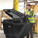 A woman in a yellow vest putting a black bag in a large black bin with a Lavex tilt truck lid.