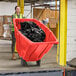 A woman in a yellow vest pushing a red Lavex trash cart full of black garbage.