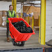 A woman in a green vest pushing a Lavex red heavy-duty tilt truck.