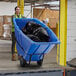 A woman pushing a Lavex blue tilt truck full of garbage.